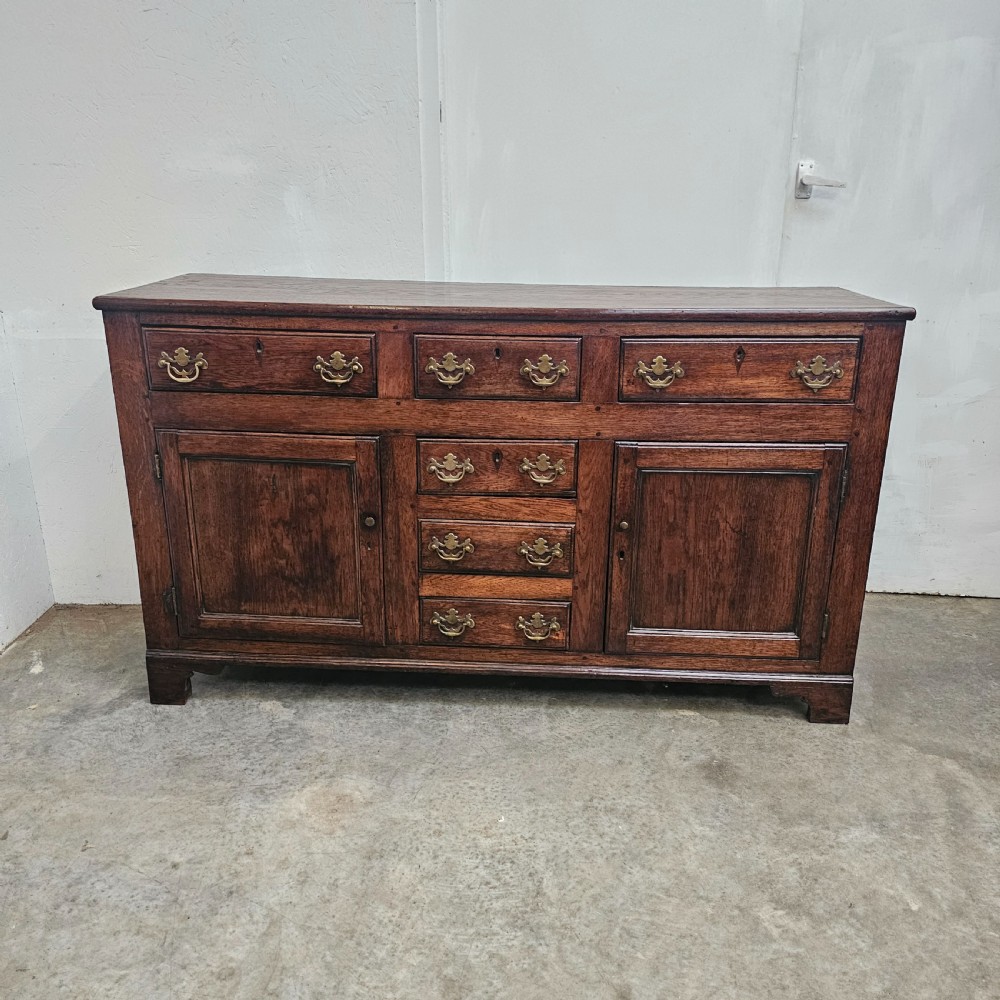 A 19th-century English oak dresser base featuring three upper drawers, three central drawers, two panelled cupboard doors, and brass swan-neck handles.