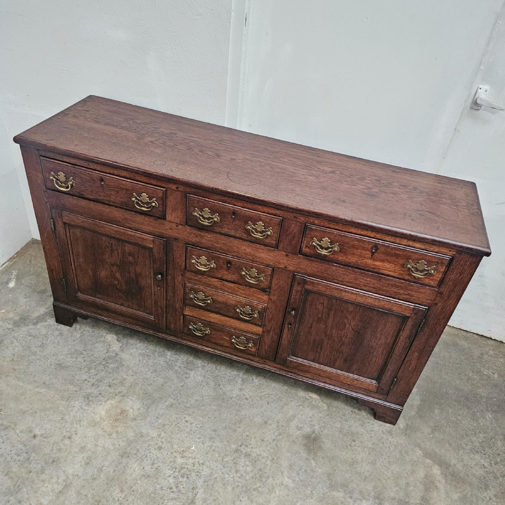A 19th-century English oak dresser base featuring three upper drawers, three central drawers, two panelled cupboard doors, and brass swan-neck handles. View II