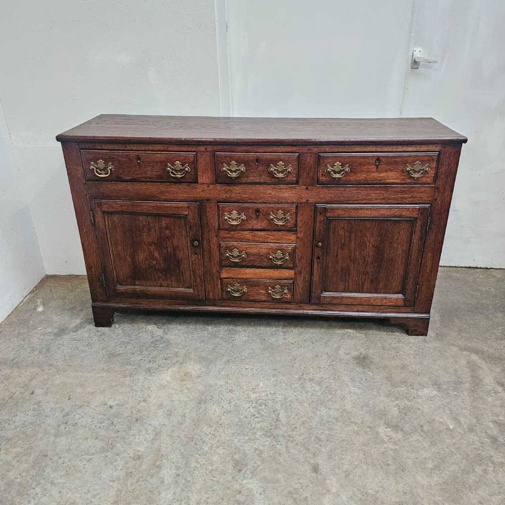 A 19th-century English oak dresser base featuring three upper drawers, three central drawers, two panelled cupboard doors, and brass swan-neck handles. View VII