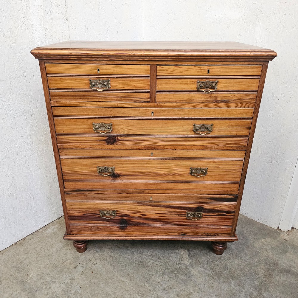 A Victorian pitch pine chest of drawers featuring two short over three long drawers with reeded details, brass handles, and turned bun feet.