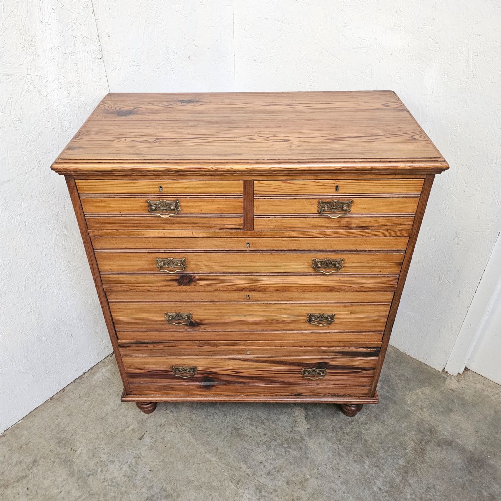 A Victorian pitch pine chest of drawers featuring two short over three long drawers with reeded details, brass handles, and turned bun feet. View II