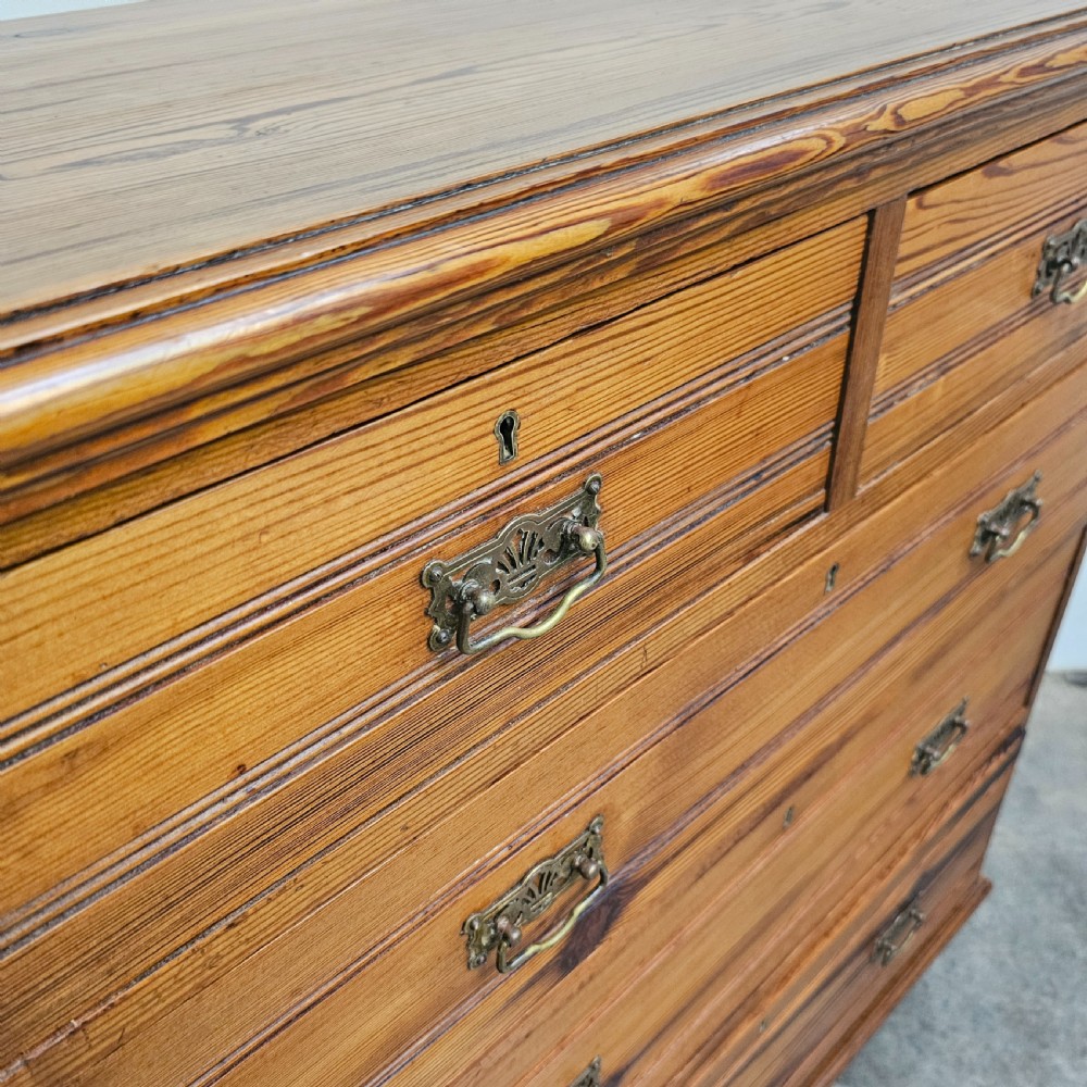 A Victorian pitch pine chest of drawers featuring two short over three long drawers with reeded details, brass handles, and turned bun feet. View V