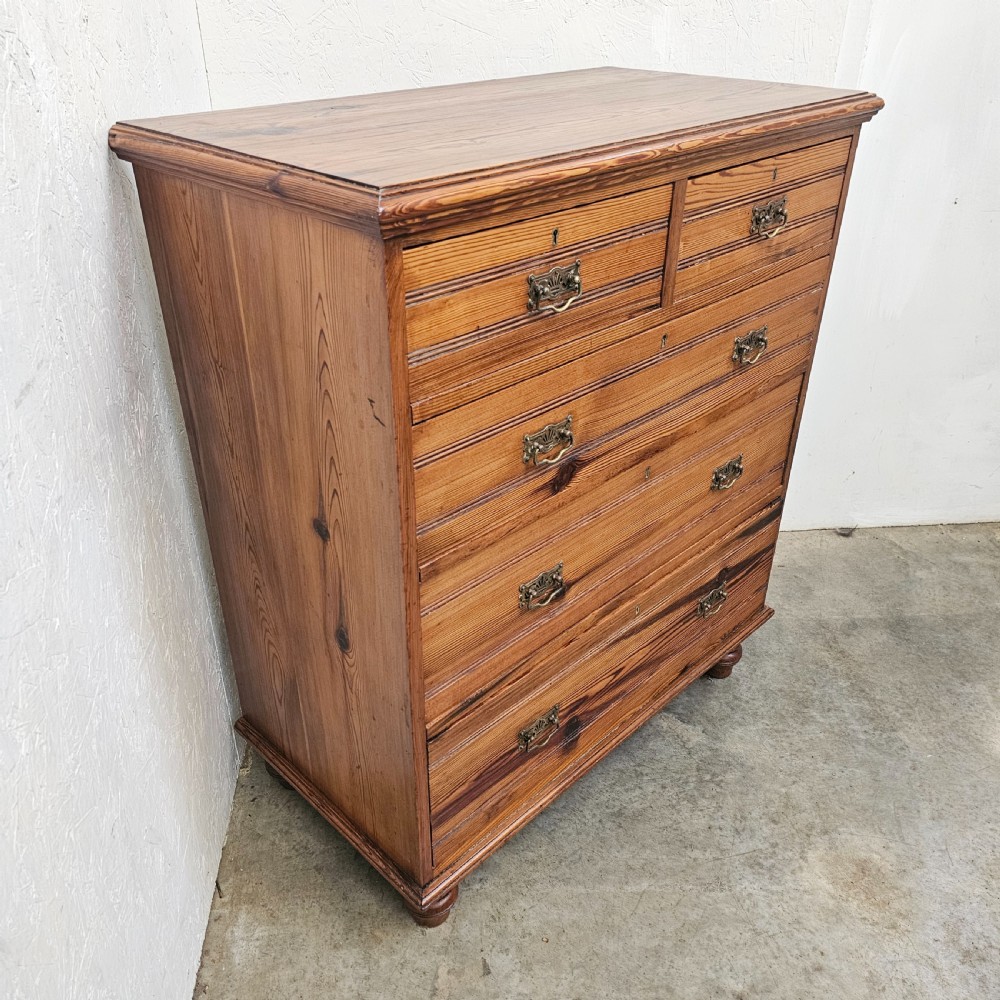 A Victorian pitch pine chest of drawers featuring two short over three long drawers with reeded details, brass handles, and turned bun feet. View VII