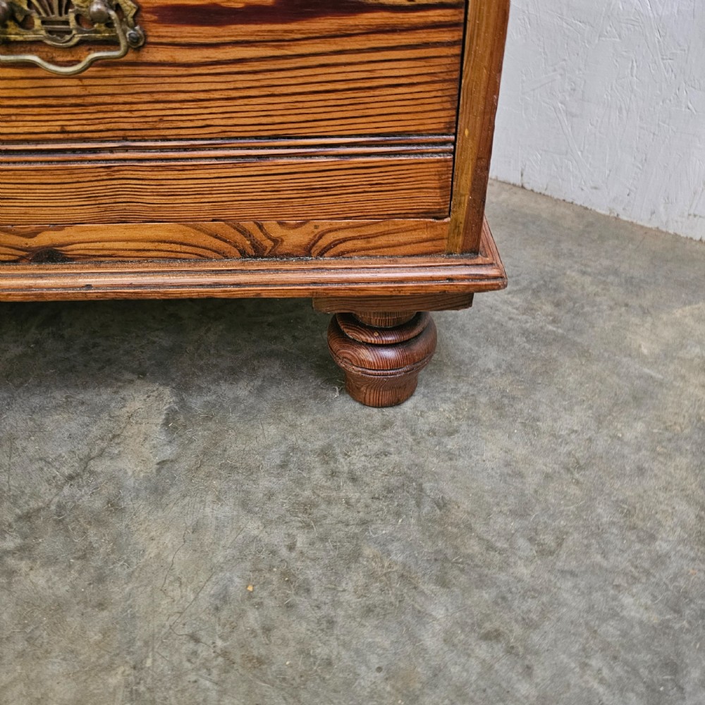 A Victorian pitch pine chest of drawers featuring two short over three long drawers with reeded details, brass handles, and turned bun feet. View X