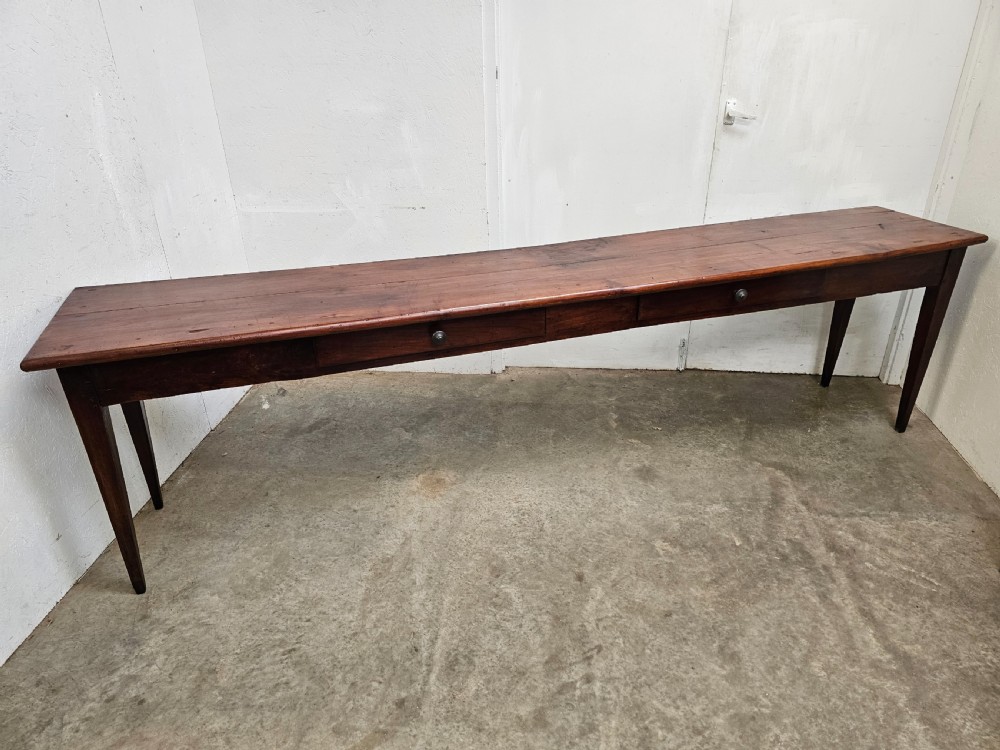 An exceptionally long French rustic wooden console table featuring two frieze drawers and simple tapered legs.