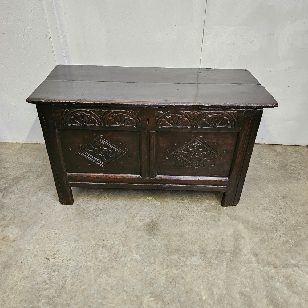 A dark oak 17th-century coffer with a two-panel front decorated with carved geometric lozenges and lunette detailing along the top rail. View II