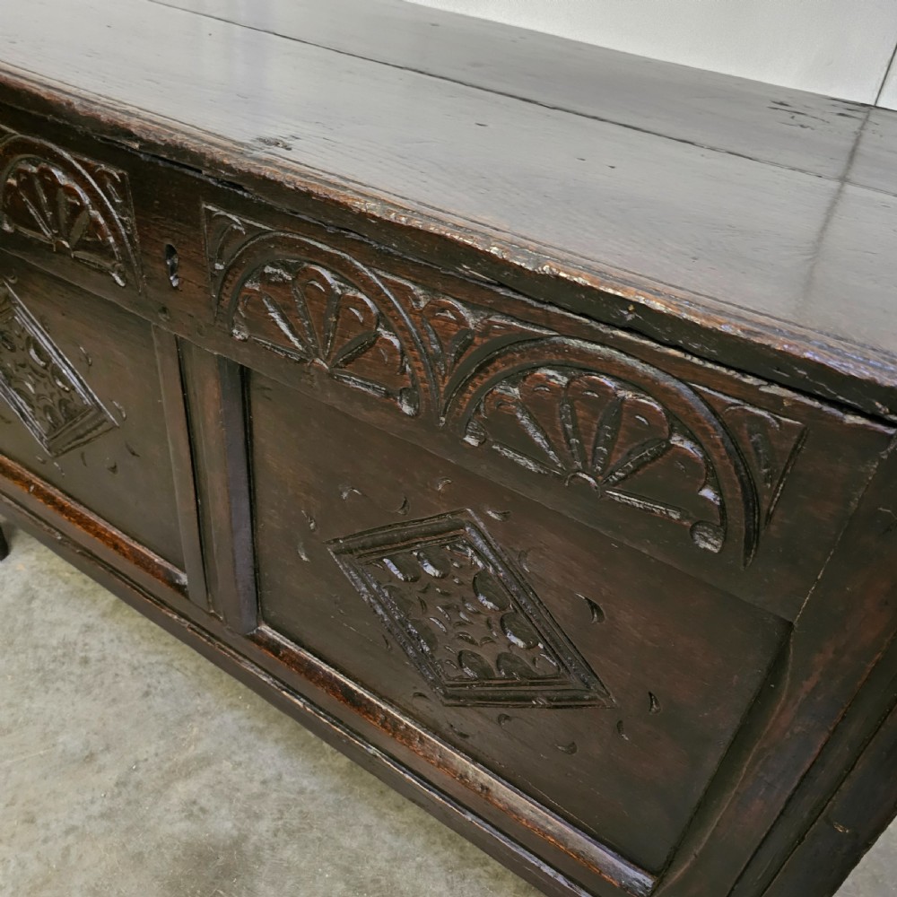 A dark oak 17th-century coffer with a two-panel front decorated with carved geometric lozenges and lunette detailing along the top rail. View III