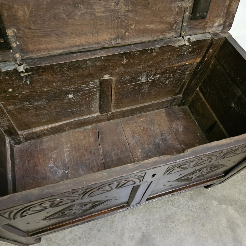 A dark oak 17th-century coffer with a two-panel front decorated with carved geometric lozenges and lunette detailing along the top rail. View V
