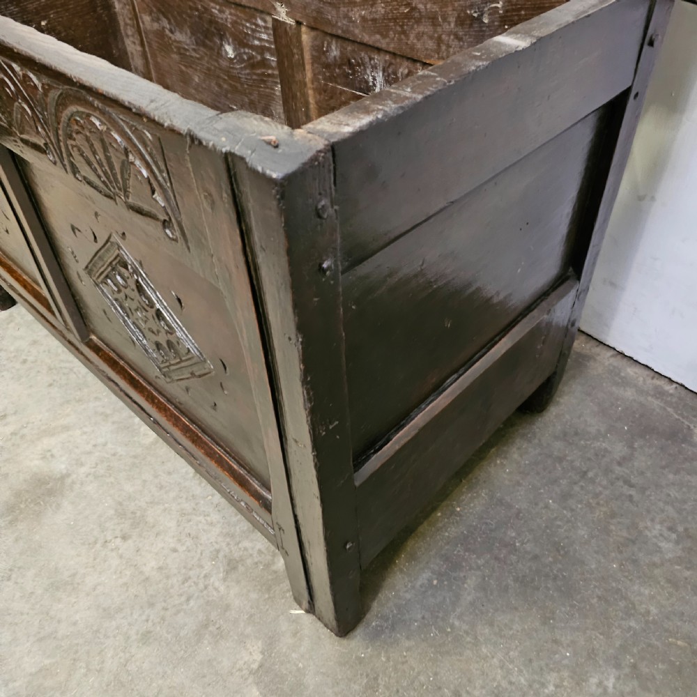 A dark oak 17th-century coffer with a two-panel front decorated with carved geometric lozenges and lunette detailing along the top rail. View VI