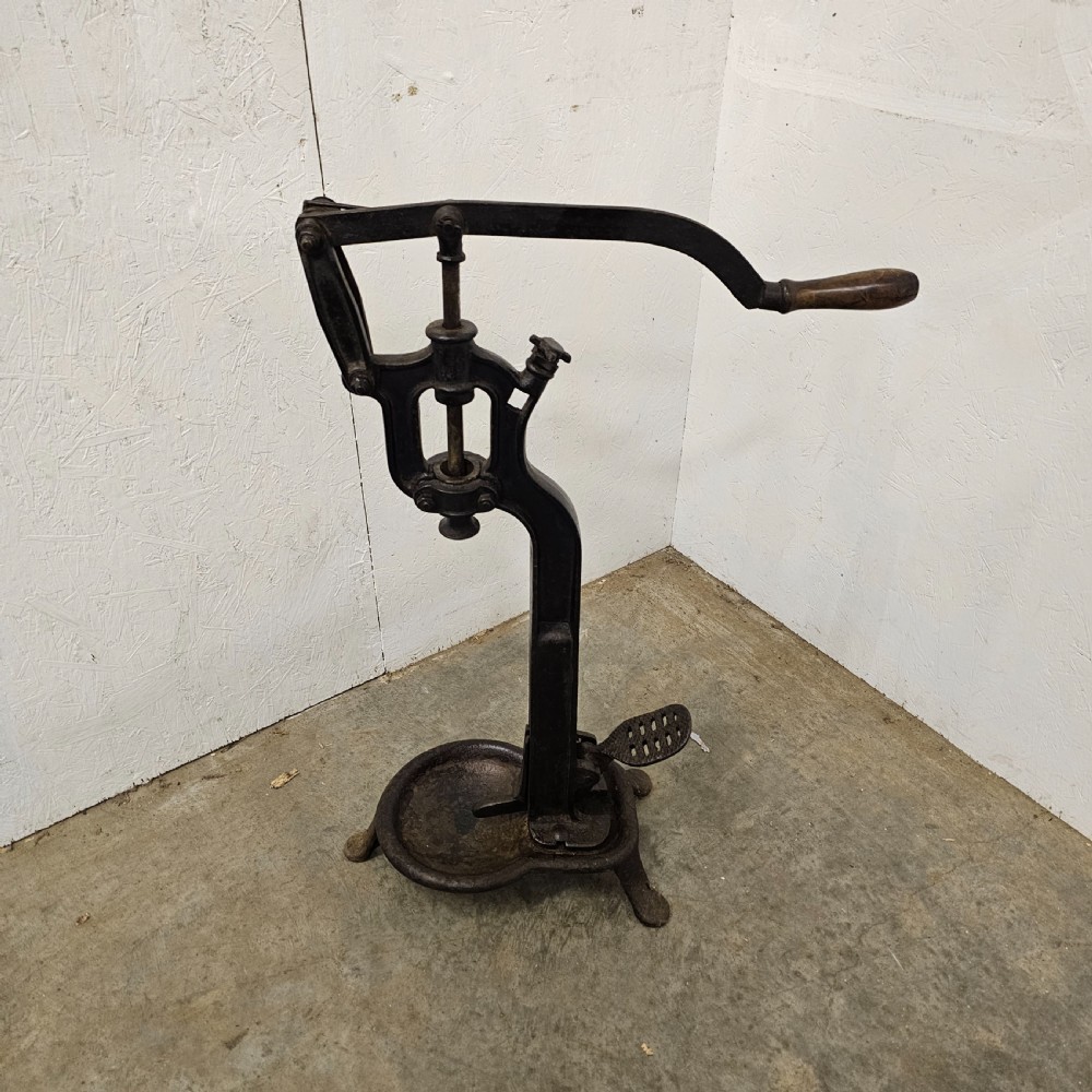 A floor-standing black cast iron antique French wine bottle corker with a long hand lever, wooden grip, plunger mechanism, and tripod base.