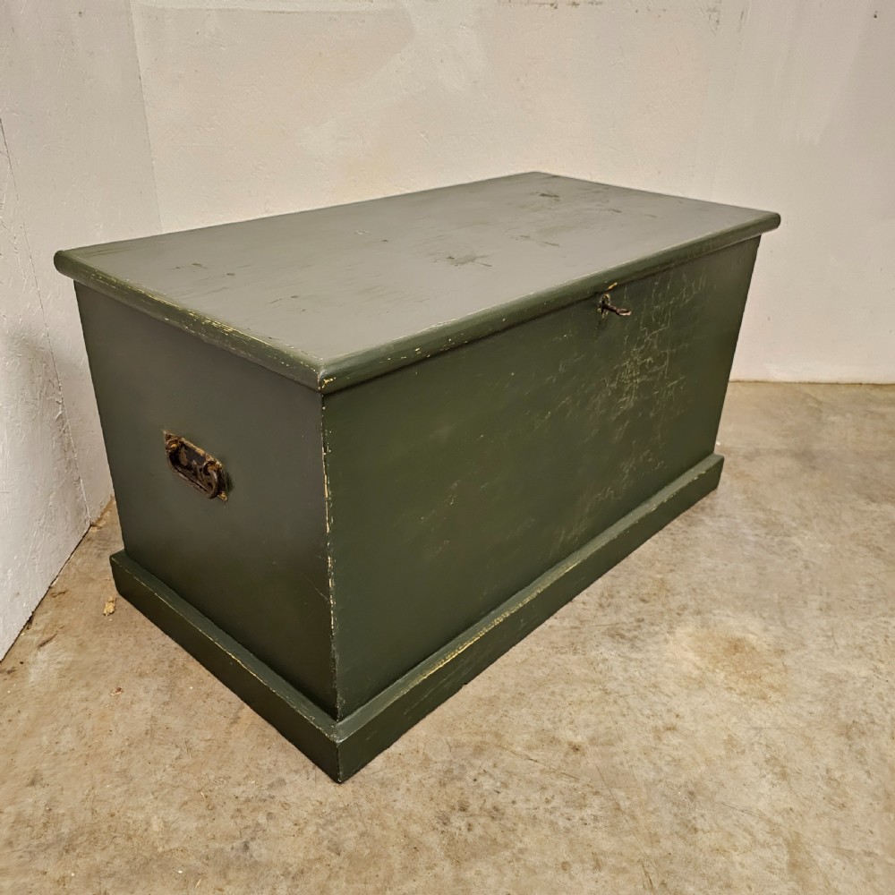 A rectangular green painted pine blanket box with side iron handles, a key in the lock, and a solid plinth base.