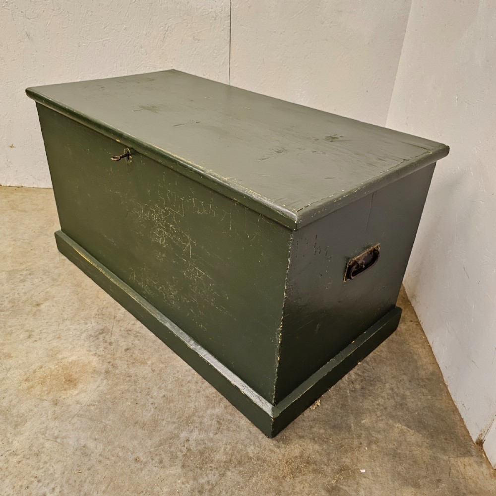 A rectangular green painted pine blanket box with side iron handles, a key in the lock, and a solid plinth base. View V