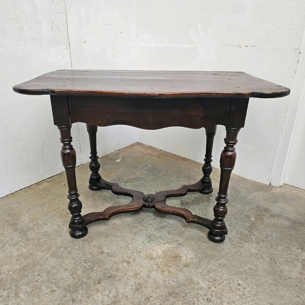 An 18th-century dark walnut side table featuring turned legs, a shaped lower apron, a moulded top, and a curved X-frame stretcher.