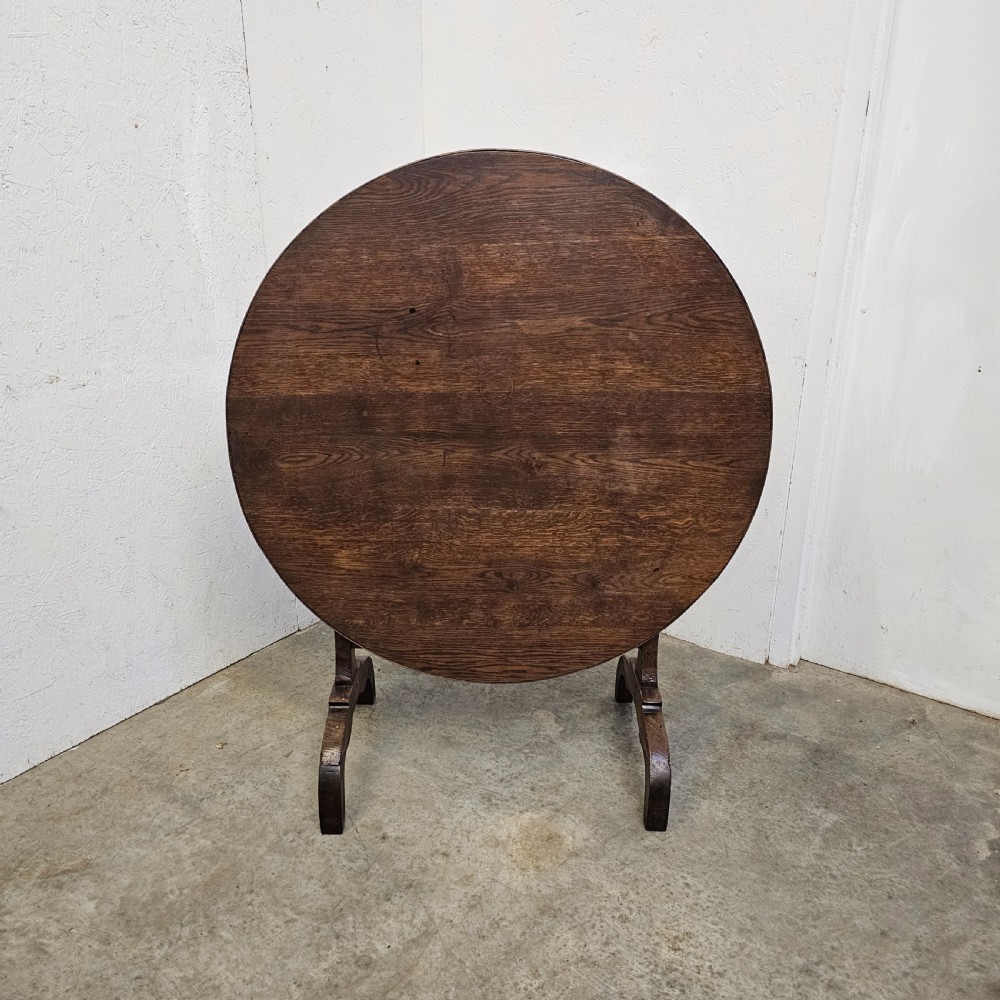 A circular dark oak vineyard table set with its top tilted vertically on a solid trestle base.
