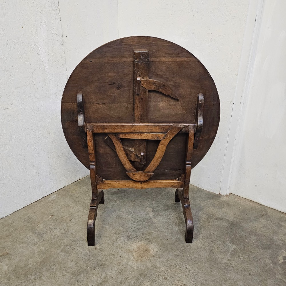 A circular dark oak vineyard table set with its top tilted vertically on a solid trestle base. View II