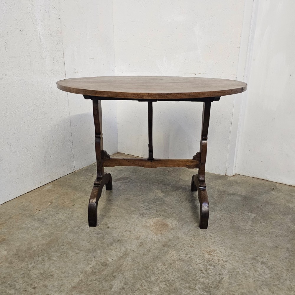A circular dark oak vineyard table set with its top tilted vertically on a solid trestle base. View III