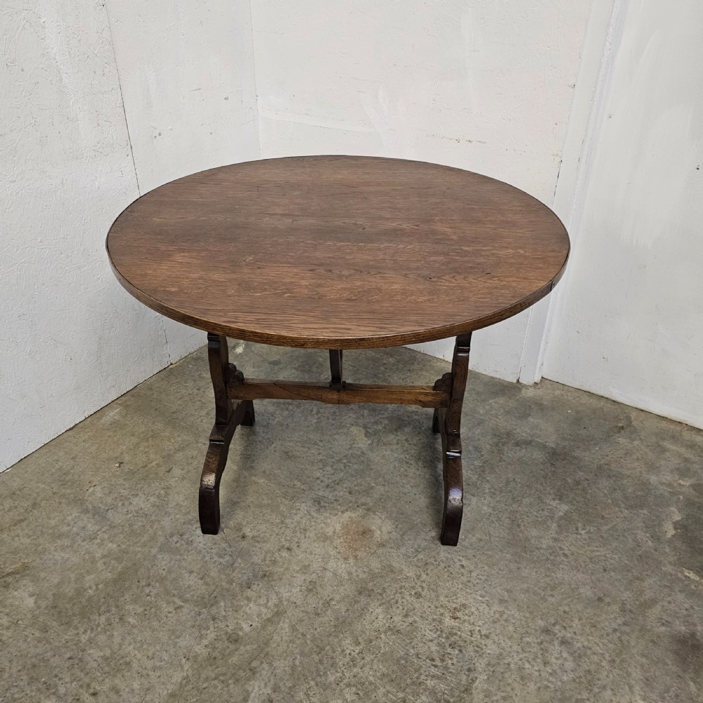A circular dark oak vineyard table set with its top tilted vertically on a solid trestle base. View IV