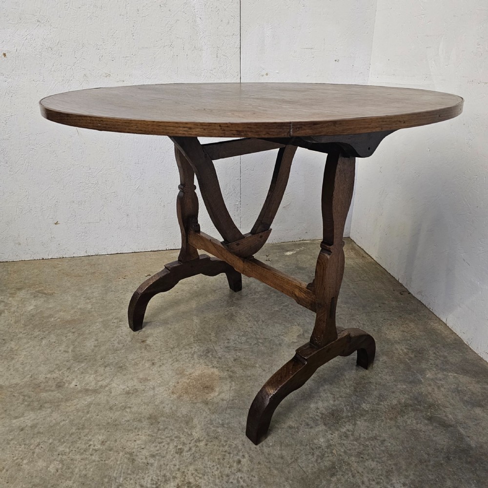 A circular dark oak vineyard table set with its top tilted vertically on a solid trestle base. View V