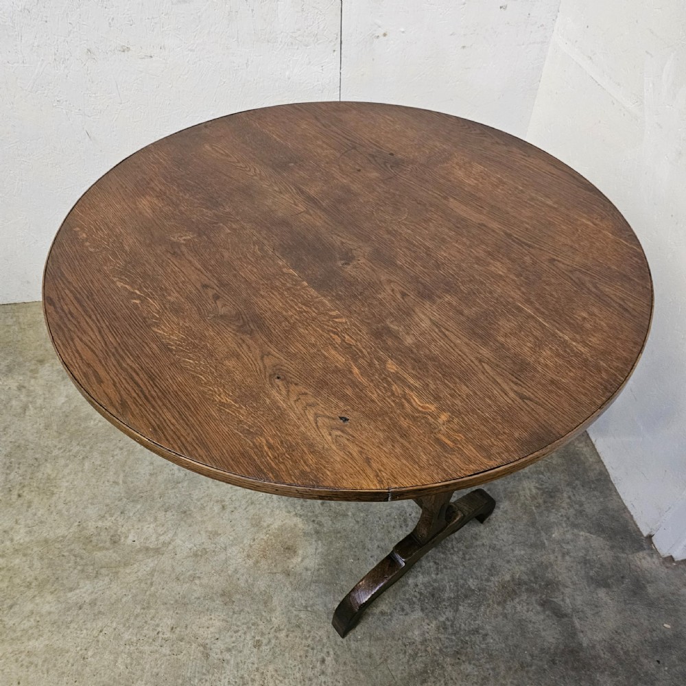 A circular dark oak vineyard table set with its top tilted vertically on a solid trestle base. View VI