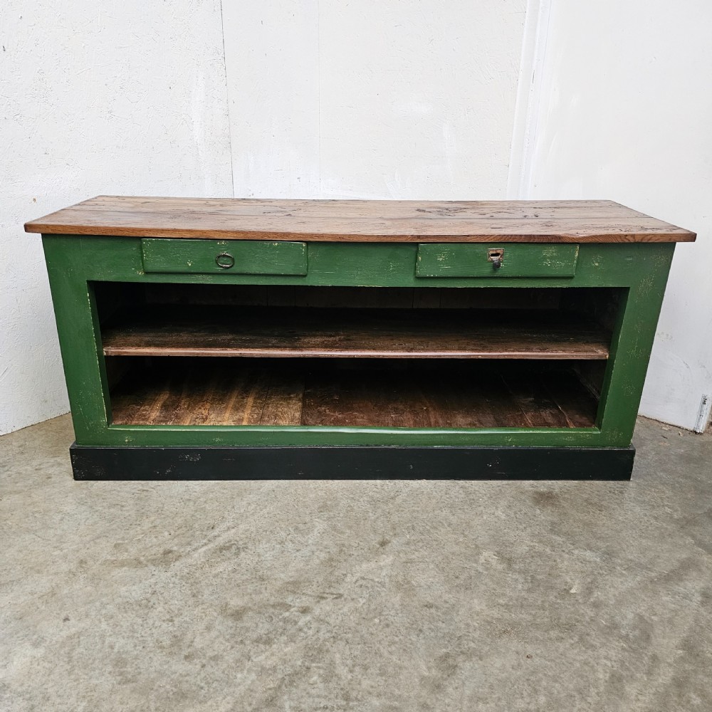 A long rustic French shop counter featuring a natural oak top, three recessed green painted front panels, and a black base plinth. View VI