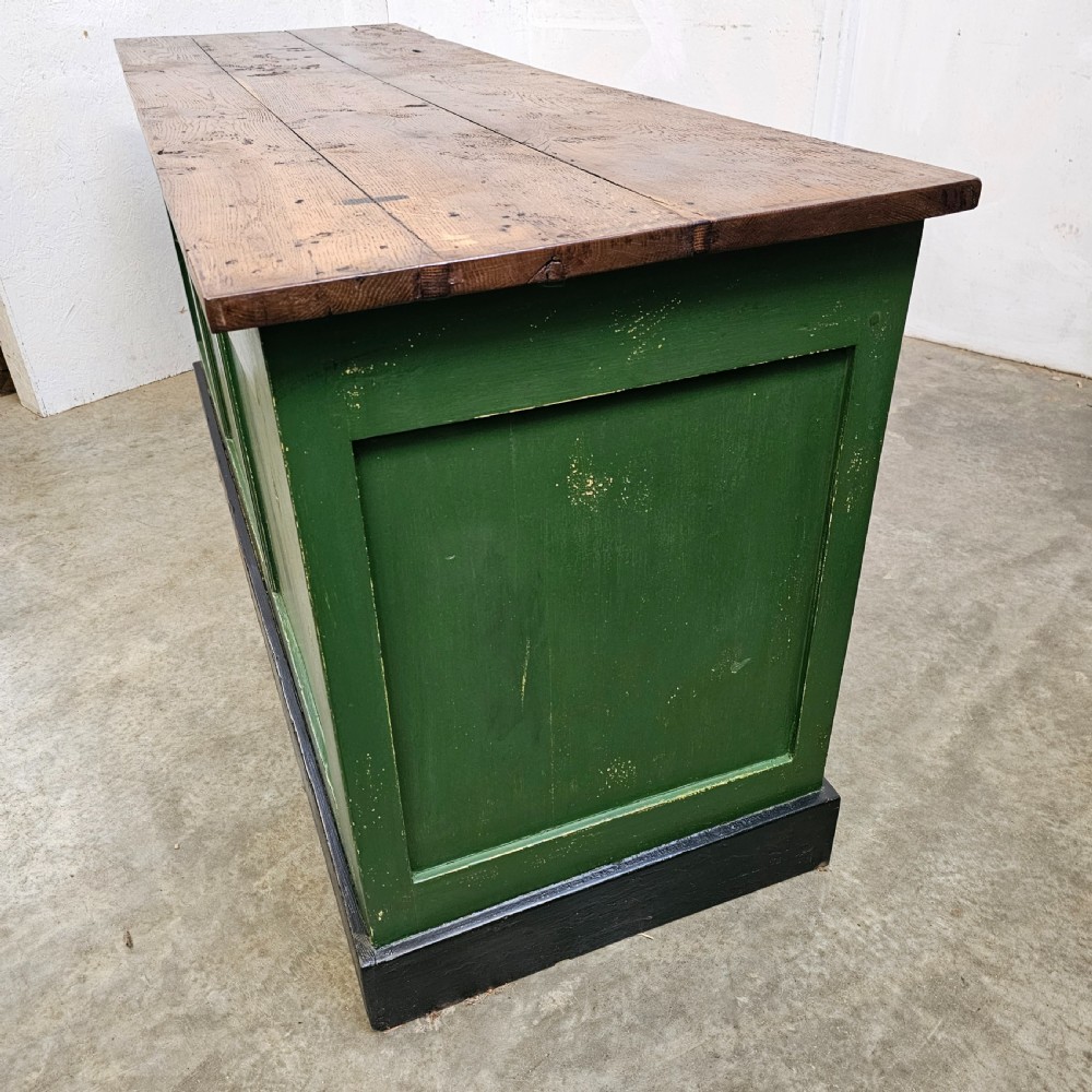 A long rustic French shop counter featuring a natural oak top, three recessed green painted front panels, and a black base plinth. View III