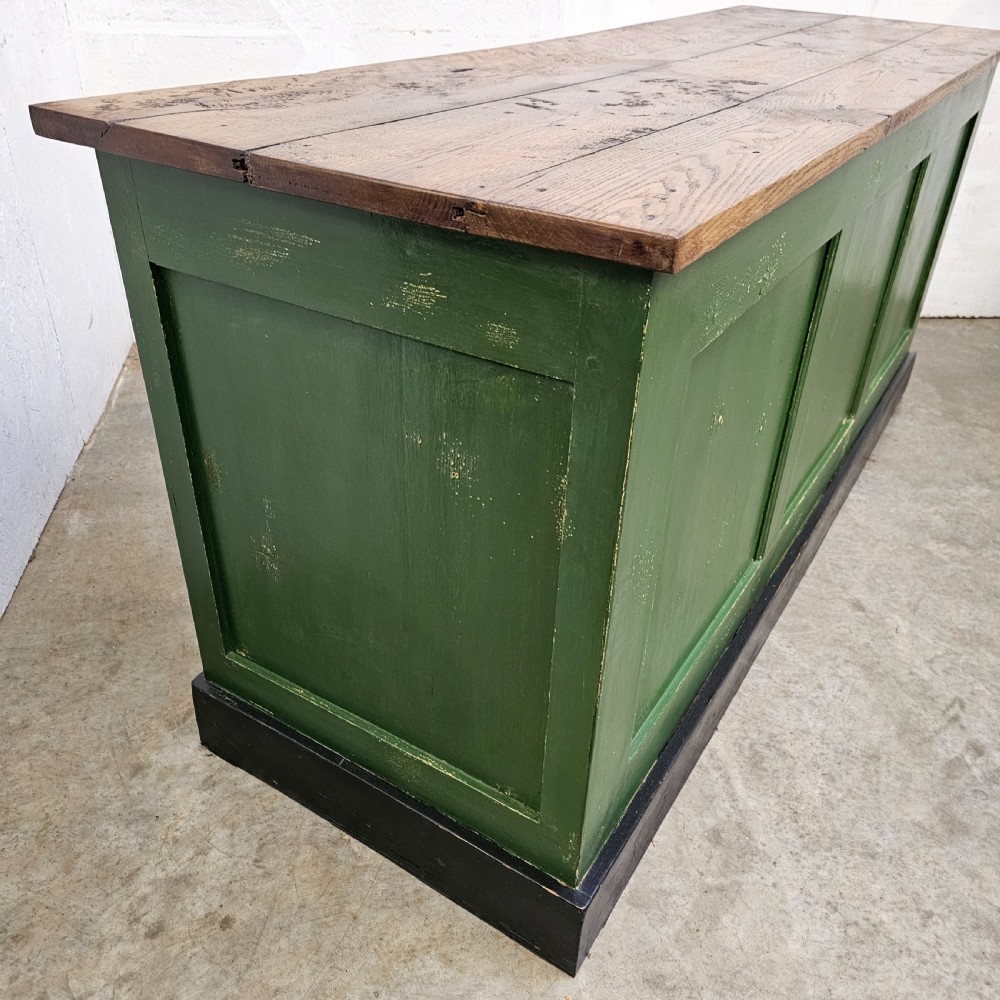 A long rustic French shop counter featuring a natural oak top, three recessed green painted front panels, and a black base plinth. View IV
