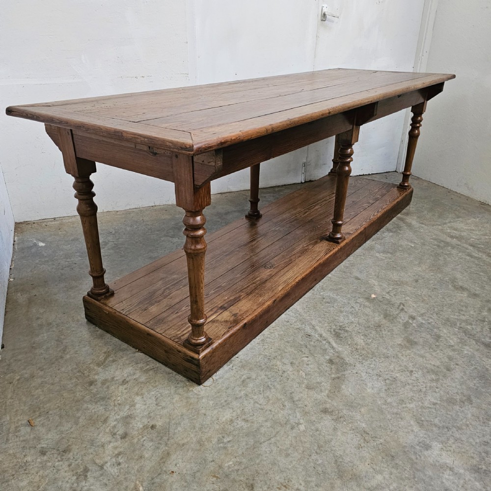 A 19th-century French pine drapers table featuring a long plank top, six turned legs, and a full-length lower pot board shelf.