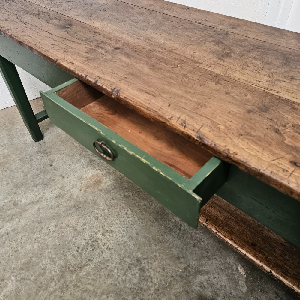 A long rustic French serving table featuring a dark green painted wooden frame, a single drawer with an iron pull, a natural wood top, and a lower pot shelf. View VI