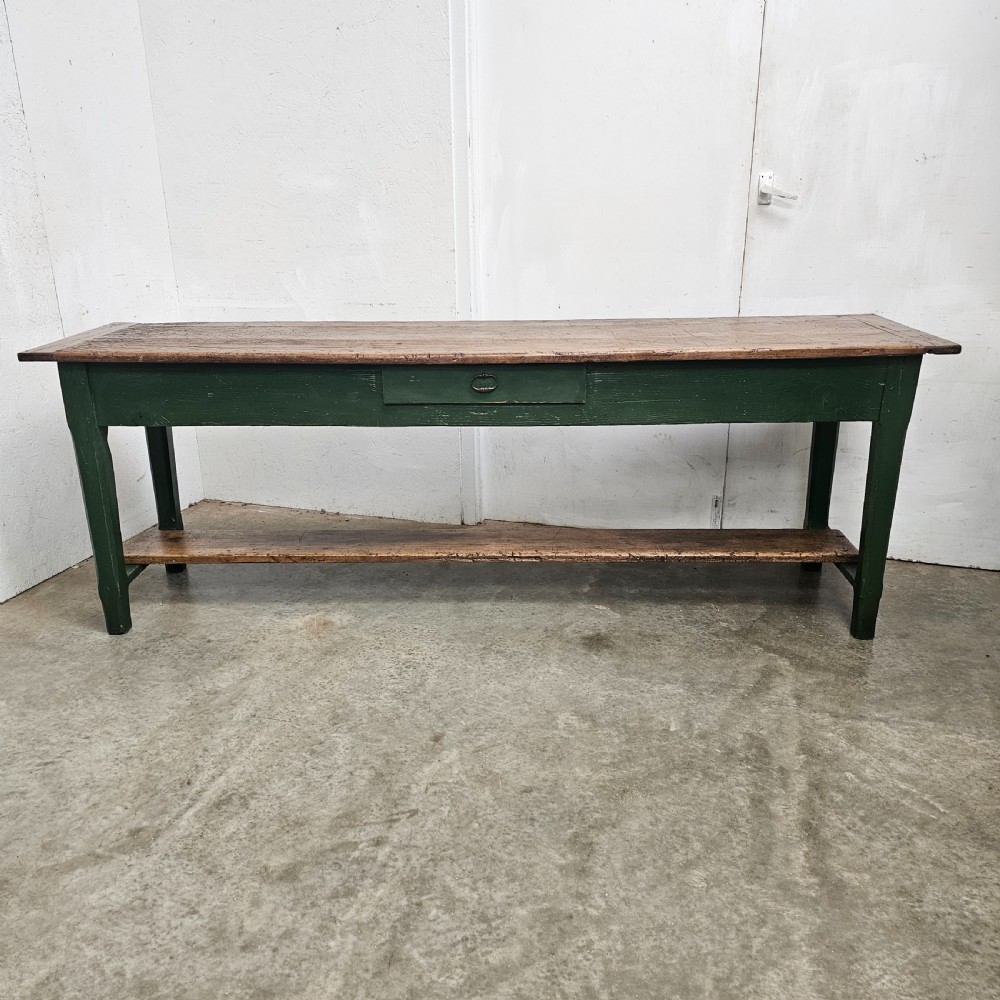 A long rustic French serving table featuring a dark green painted wooden frame, a single drawer with an iron pull, a natural wood top, and a lower pot shelf.