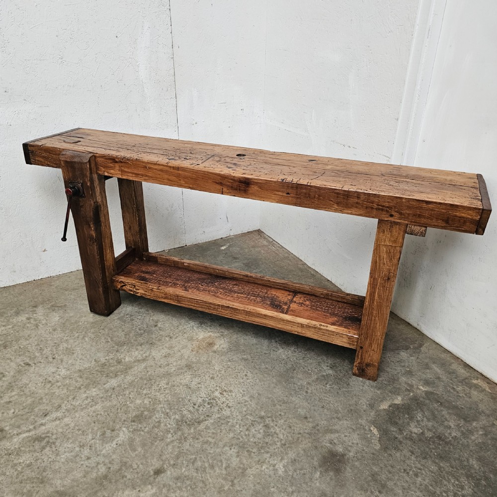 A rustic French wooden workbench featuring a thick plank top, lower shelf, and integrated vice on the left leg. View II