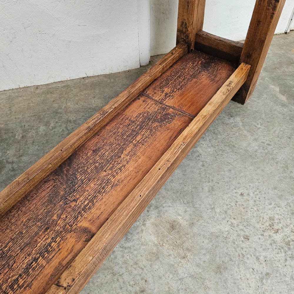 A rustic French wooden workbench featuring a thick plank top, lower shelf, and integrated vice on the left leg. View III