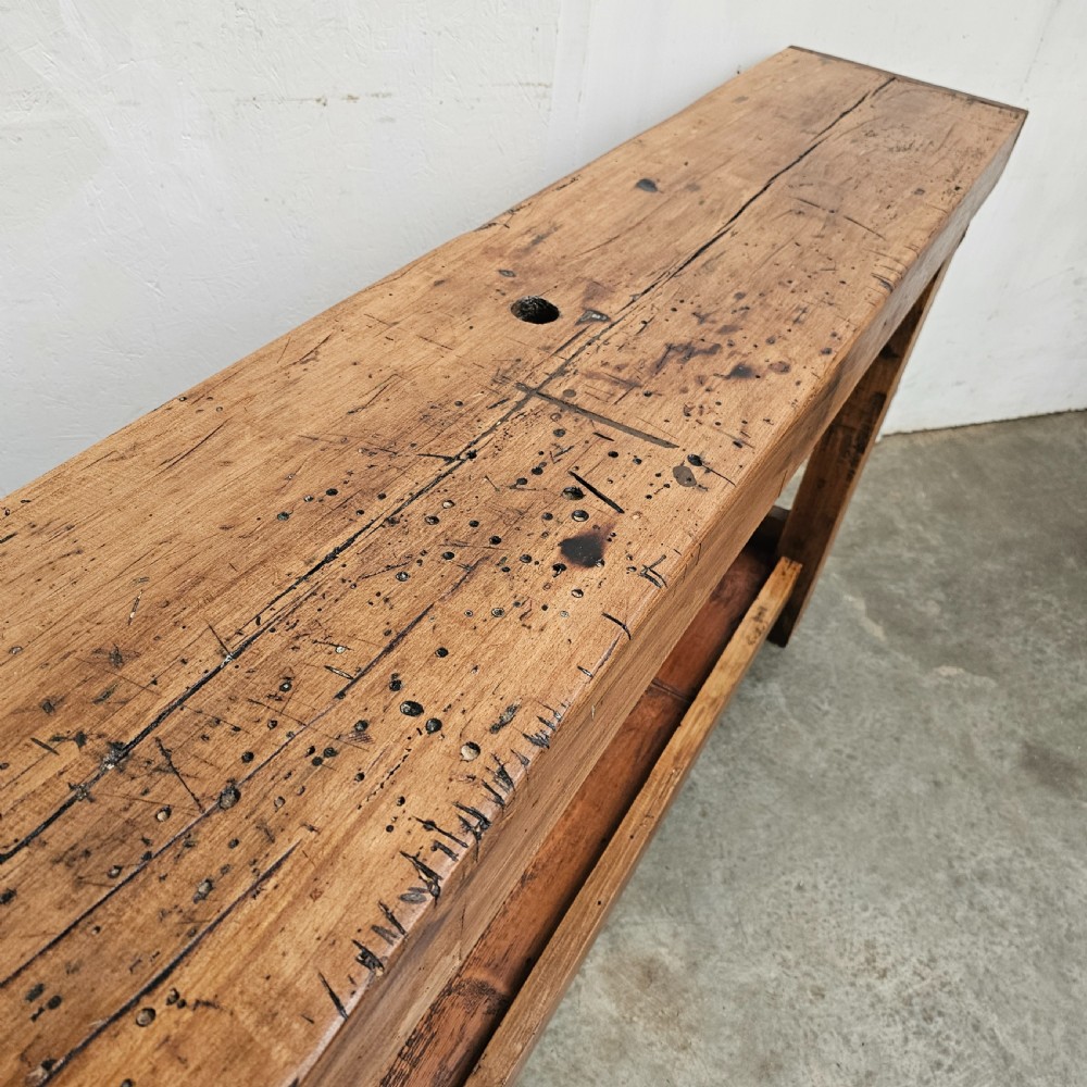 A rustic French wooden workbench featuring a thick plank top, lower shelf, and integrated vice on the left leg. View IV