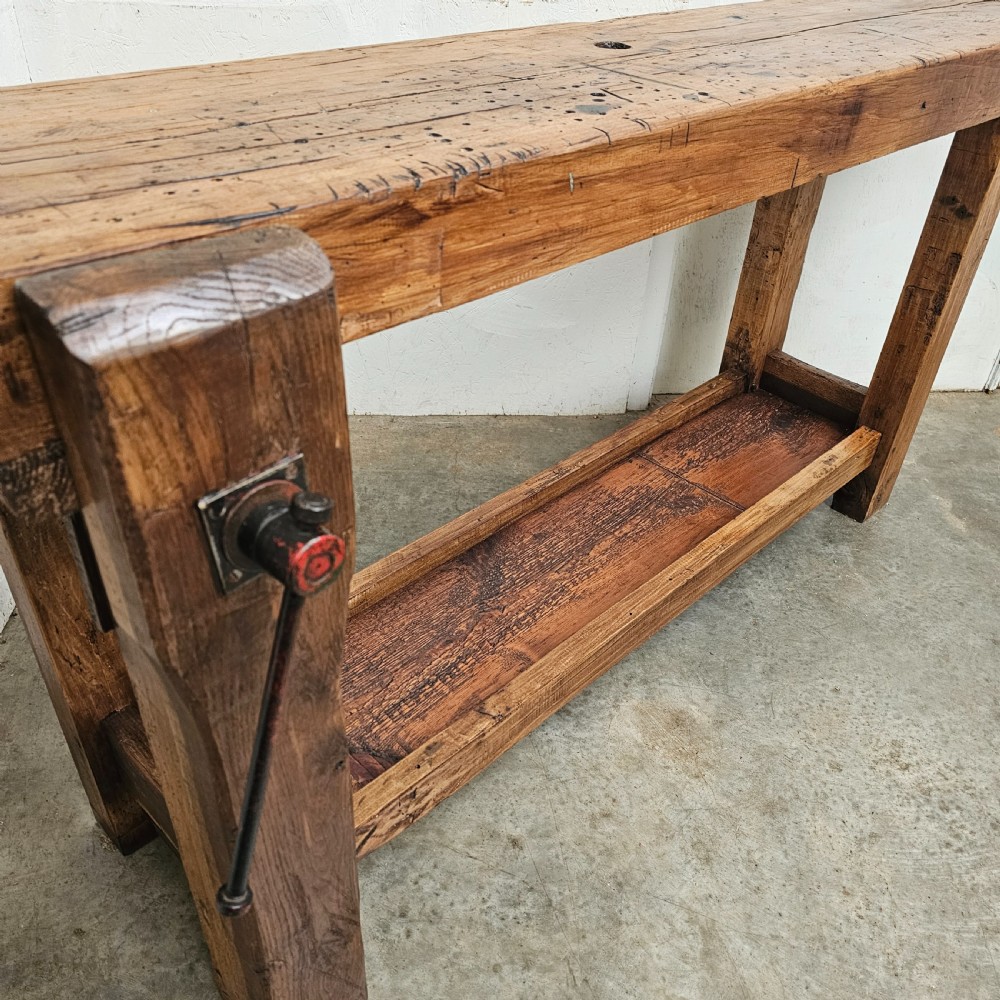 A rustic French wooden workbench featuring a thick plank top, lower shelf, and integrated vice on the left leg. View V