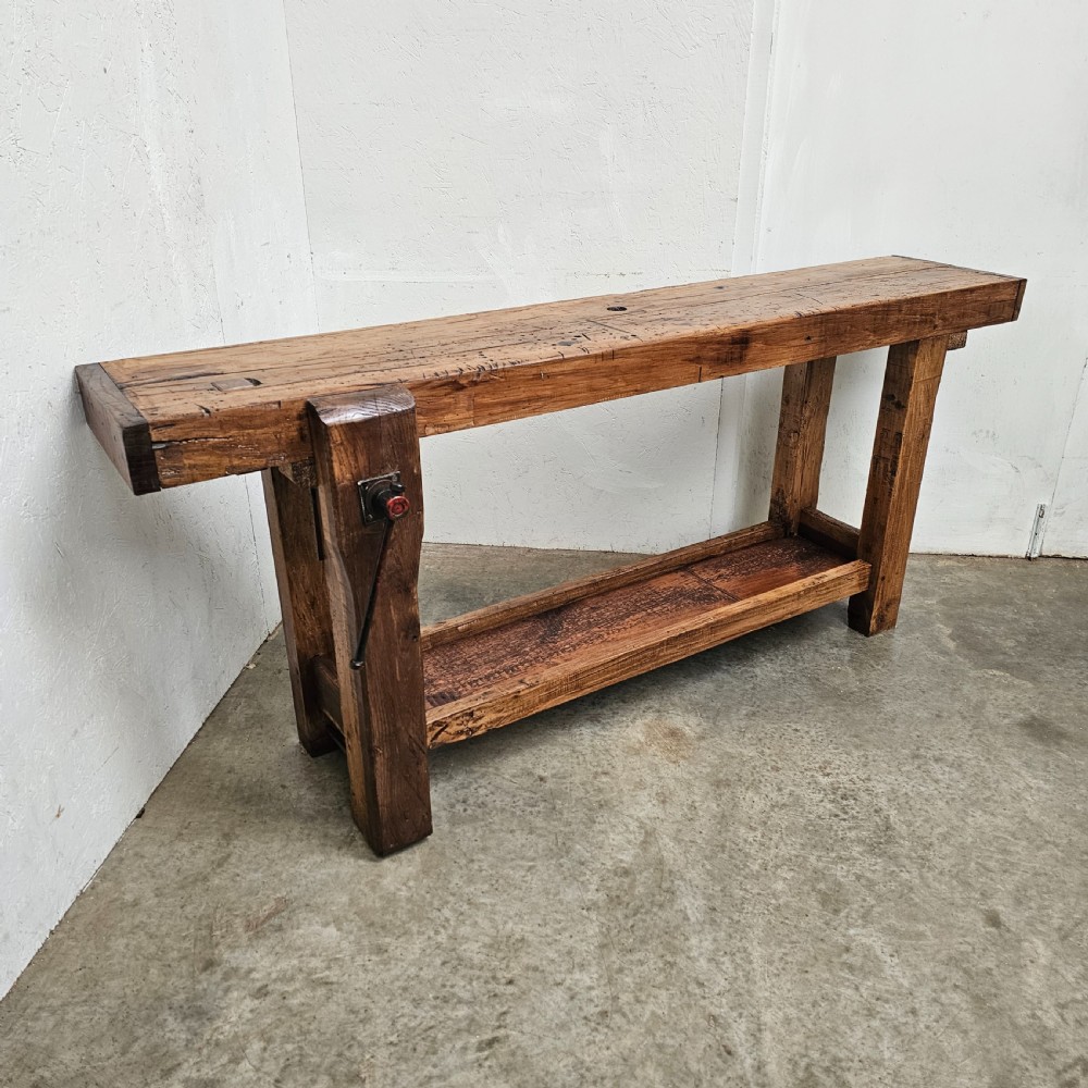 A rustic French wooden workbench featuring a thick plank top, lower shelf, and integrated vice on the left leg. View VII