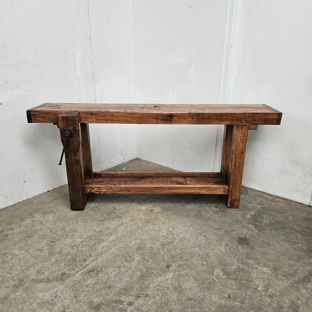 A rustic French wooden workbench featuring a thick plank top, lower shelf, and integrated vice on the left leg. View VIII