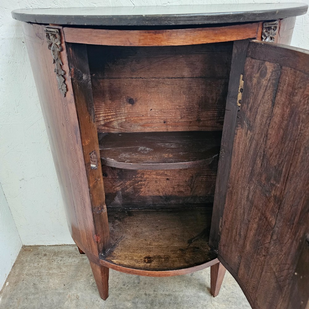 A French Louis XVI style demi-lune console cabinet featuring dark wood finish, floral marquetry inlay on the single door, dark marble top, and tapered legs. View VIII