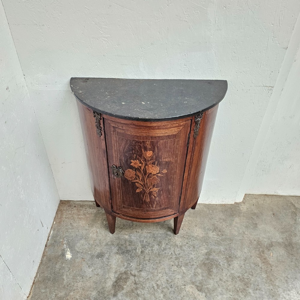 A French Louis XVI style demi-lune console cabinet featuring dark wood finish, floral marquetry inlay on the single door, dark marble top, and tapered legs. View V