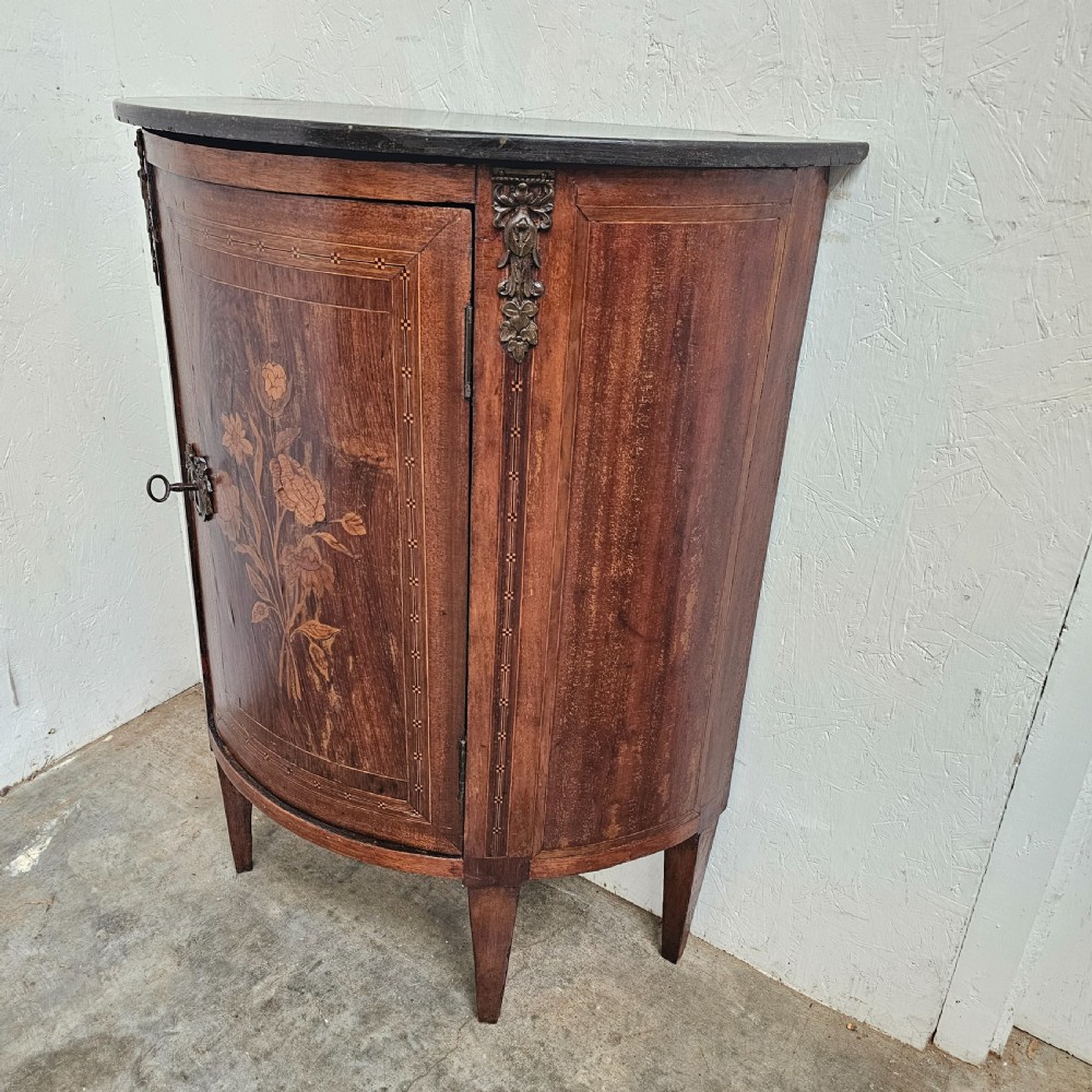 A French Louis XVI style demi-lune console cabinet featuring dark wood finish, floral marquetry inlay on the single door, dark marble top, and tapered legs. View VI