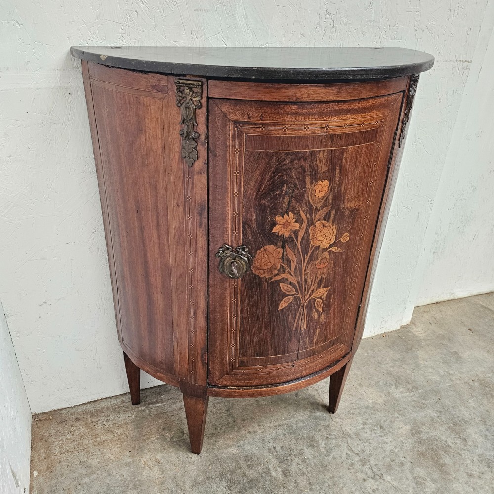 A French Louis XVI style demi-lune console cabinet featuring dark wood finish, floral marquetry inlay on the single door, dark marble top, and tapered legs. View VII