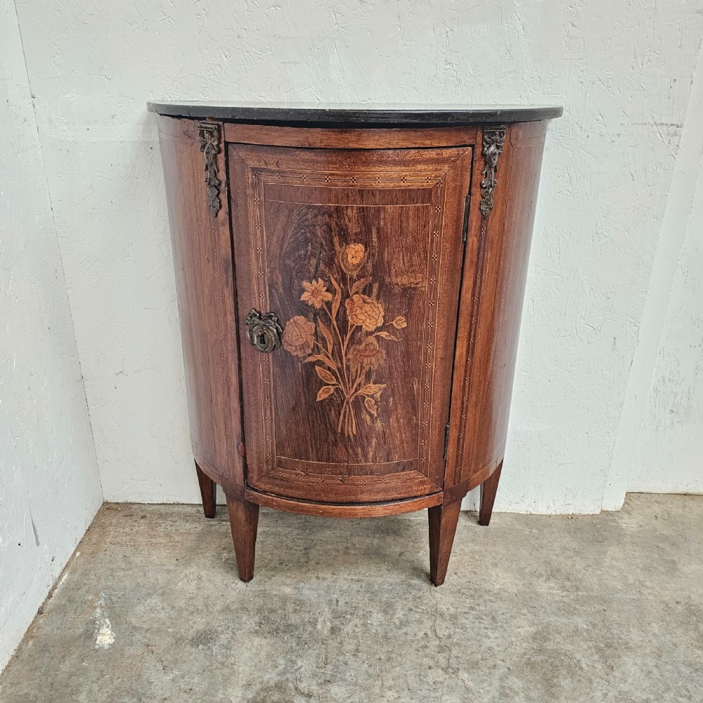 A French Louis XVI style demi-lune console cabinet featuring dark wood finish, floral marquetry inlay on the single door, dark marble top, and tapered legs.