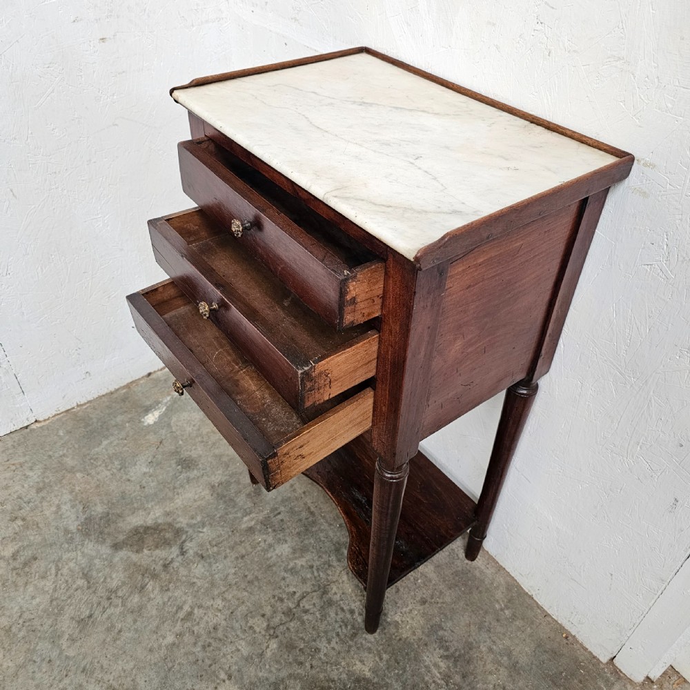 An antique French dark walnut bedside chest featuring an inset white marble top, three stacked drawers with metal rosette knobs, turned legs, and a lower undertier shelf. View VI