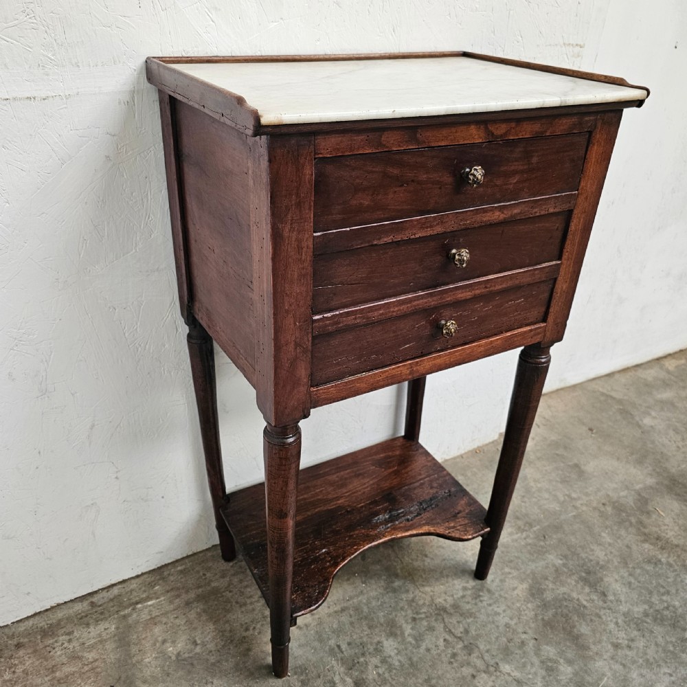 An antique French dark walnut bedside chest featuring an inset white marble top, three stacked drawers with metal rosette knobs, turned legs, and a lower undertier shelf. View II