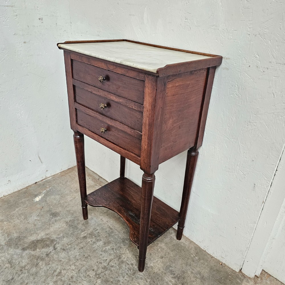 An antique French dark walnut bedside chest featuring an inset white marble top, three stacked drawers with metal rosette knobs, turned legs, and a lower undertier shelf. View IV