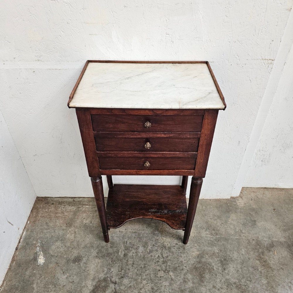 An antique French dark walnut bedside chest featuring an inset white marble top, three stacked drawers with metal rosette knobs, turned legs, and a lower undertier shelf. View V