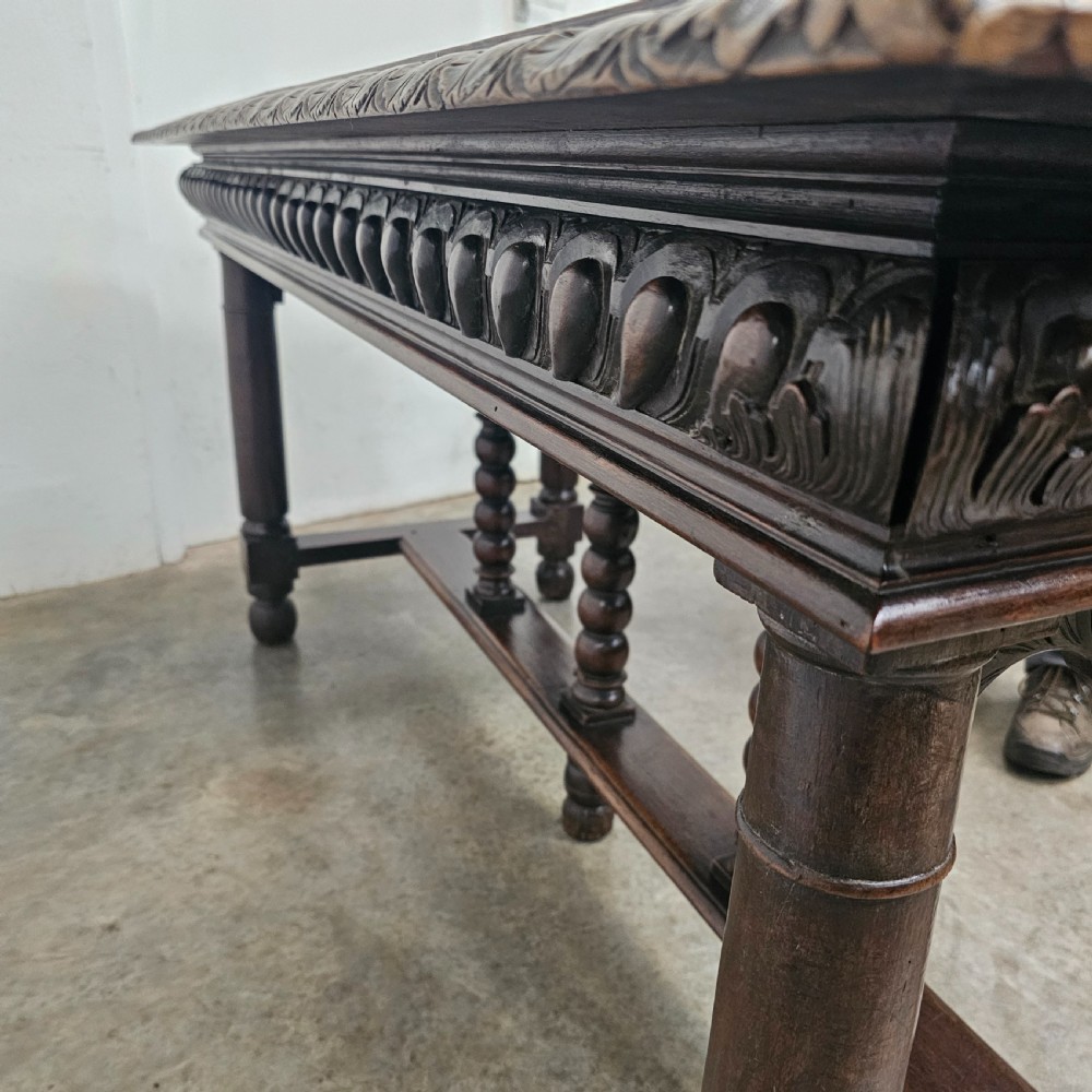 A rectangular dark walnut centre table featuring a deeply carved egg-and-dart frieze, turned column legs, and a central stretcher with spindle supports. View IX