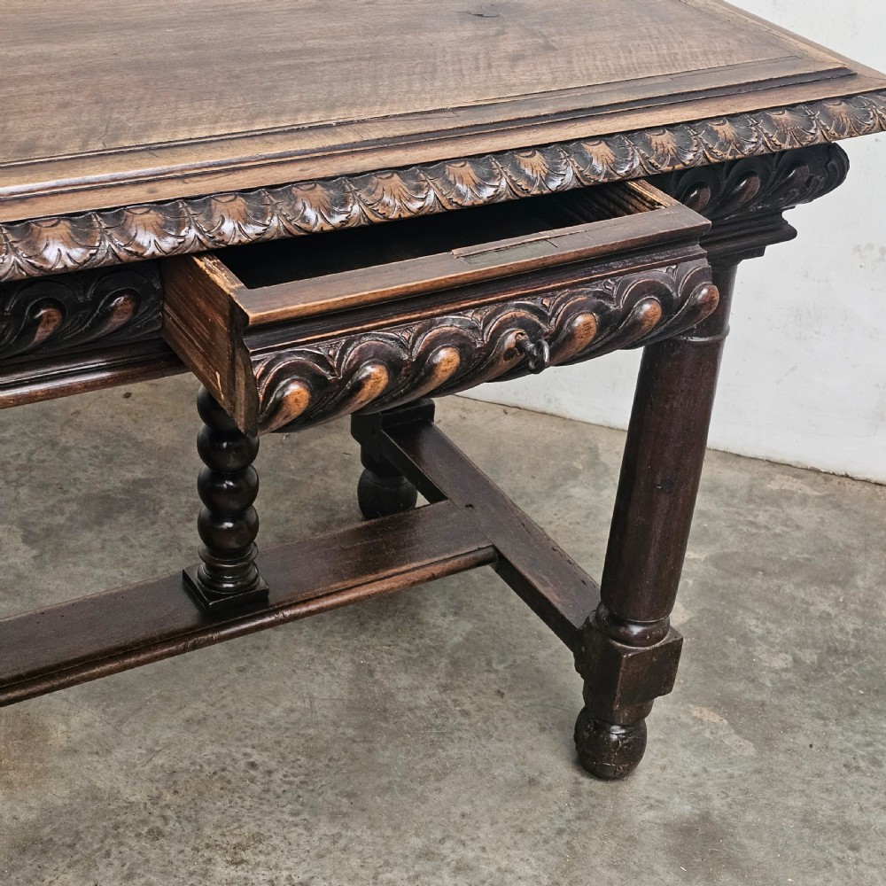 A rectangular dark walnut centre table featuring a deeply carved egg-and-dart frieze, turned column legs, and a central stretcher with spindle supports. View VI