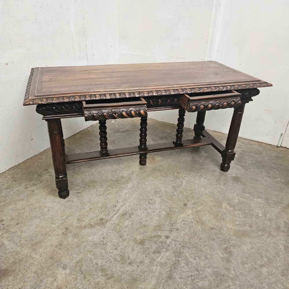 A rectangular dark walnut centre table featuring a deeply carved egg-and-dart frieze, turned column legs, and a central stretcher with spindle supports. View VII