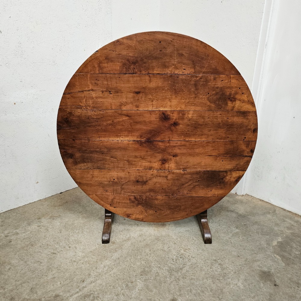 A large circular cherry wood plank table top resting on an oak trestle base in a tilted vertical orientation.