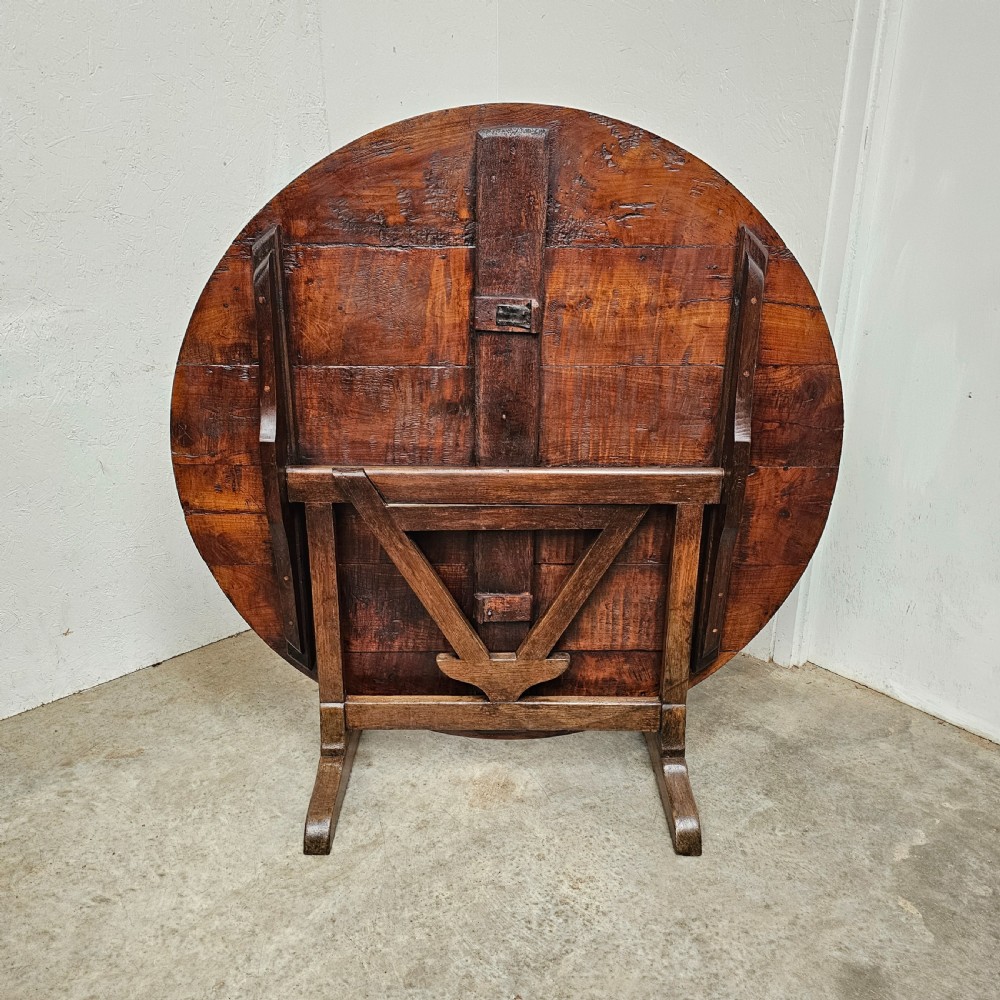 A large circular cherry wood plank table top resting on an oak trestle base in a tilted vertical orientation. View VI