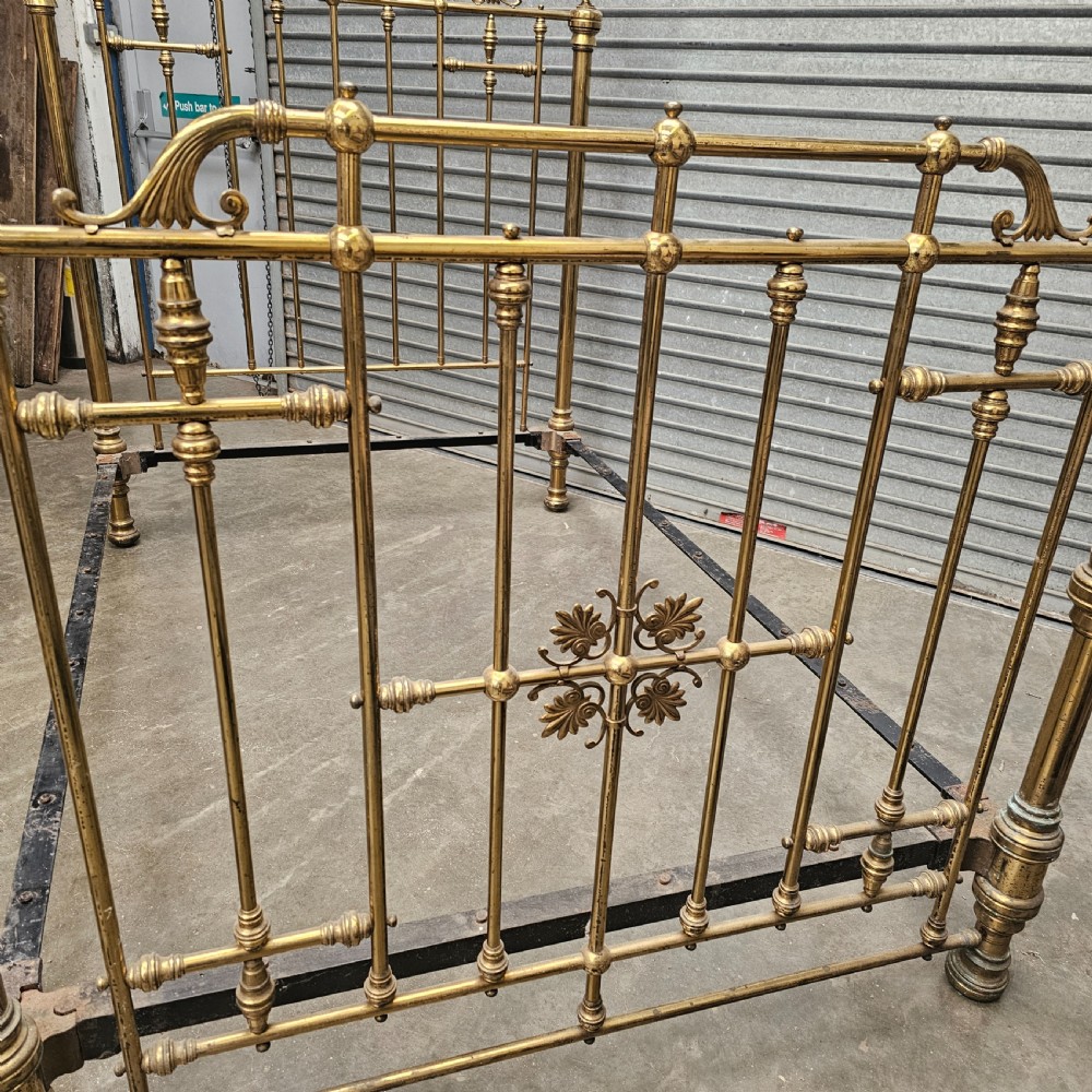 An antique Victorian double bed frame crafted with vertical brass spindles, decorative brass rosettes, turned urn finials, and a black cast iron base. View III